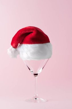 Pembe arka planda Noel Baba şapkası olan martini bardağı. Minimum Noel teması. Yeni yıl partisi konsepti.