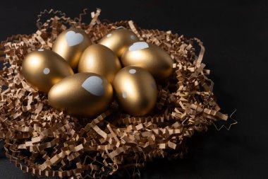 Siyah arka planda kağıt yuvadaki altın yumurtalar.