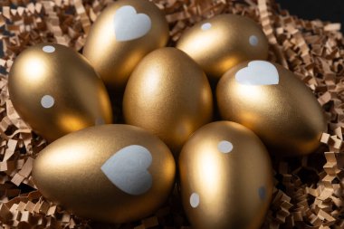 Koyu bir masanın üzerindeki kağıt yuvadaki altın yumurtaların yakın görüntüsü.