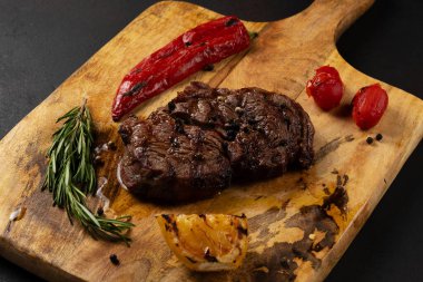 Izgara kaburga gözü. Siyah Angus. Ahşap tahtada, siyah arka planda biber ve otlarla servis ediliyor..