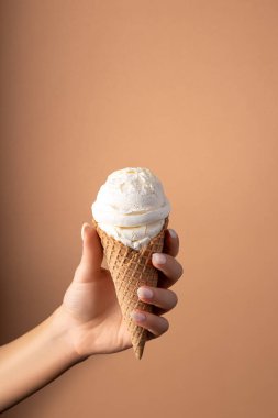 Beyaz dondurma kepçesi, elinde parlak bir arka planda dondurma külahıyla. Asgari yaz konsepti.