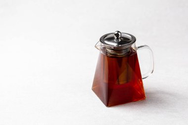 Beyaz zemin üzerinde sıcak siyah çay olan cam çaydanlık.