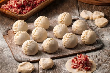 Semi-finished manti oriental dumplings on wooden board with flour