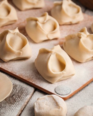 Semi-finished manti oriental dumplings on wooden board with flour