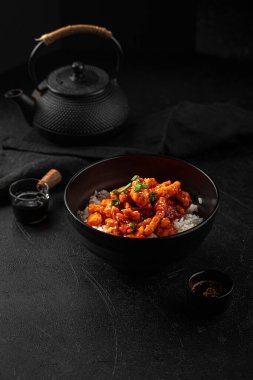 Siyah zemin üzerinde pirinç olan Asya baharatlı ballı tavuk porsiyonu.