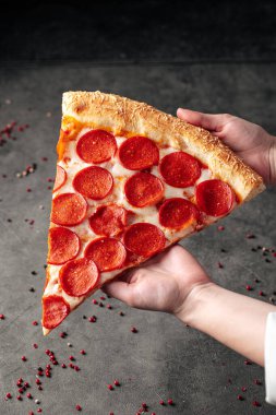 Elleri büyük bir dilim pepperonili pizza tutuyor.