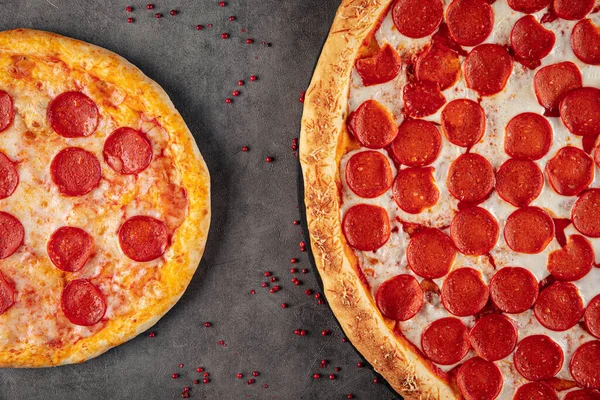Side view on small and giant pepperoni pizzas on grey background