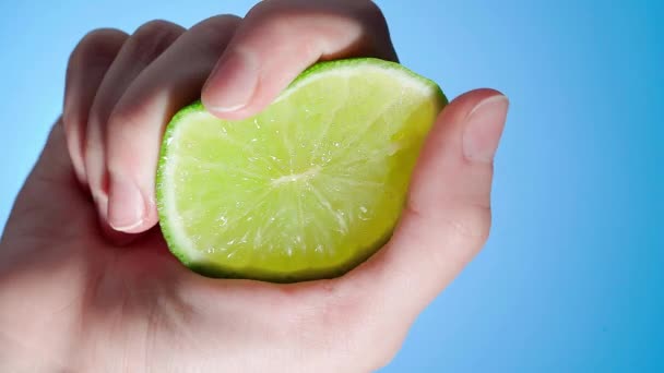 Hand Squeezes Lime Slice Juice Flows Out Blue Background — Stock Video