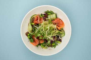 Mavi arka planda somonlu taze gurme salatası.