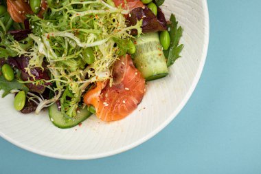 Mavi arka planda somonlu taze gurme salatası.