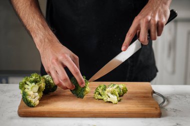 Ahşap bir tahtada brokoli kesen şef sağlıklı bir yemek hazırlıyor.