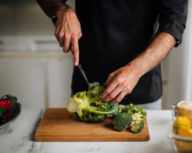Ahşap bir tahtada brokoli kesen şef sağlıklı bir yemek hazırlıyor.