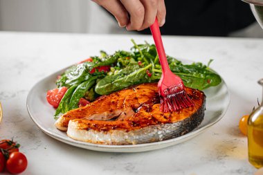 Şef somon balığı bifteğine sos sürüyor.