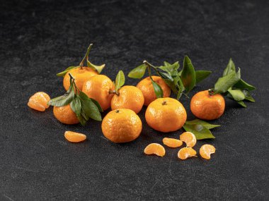 Gri arkaplanda yaprakları olan olgun mandalina meyveleri.