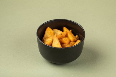 Yeşil arka planda siyah kasede fırınlanmış patates parçaları.