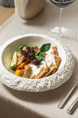 Beyaz soslu hindi şnitzel ve beyaz tabakta ızgara sebze.