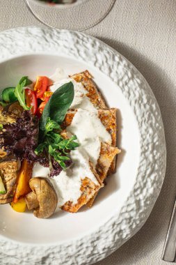 Beyaz soslu hindi şnitzel ve beyaz tabakta ızgara sebze.