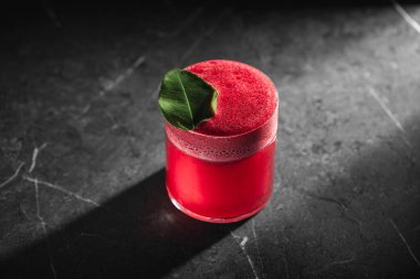 Kırmızı meyve kokteyli köpüklü ve yeşil yapraklı koyu taş arka planda garnitür