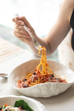 Domates soslu ve beyaz kasede zeytinli spagetti çeviren kadın.