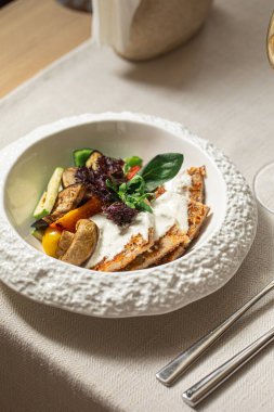 Beyaz soslu hindi şnitzel ve beyaz tabakta ızgara sebze.