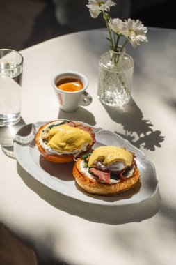 Güneşli sabah kahvaltısı Benedict yumurtaları ve espresso ile masada.