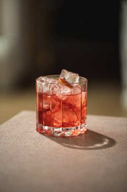 Buz küplü kırmızı kokteyl ve tezgahta küçük bardakta turuncu bükülme.