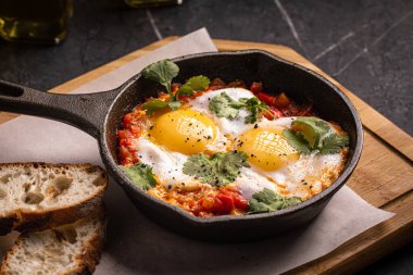Haşlanmış yumurta ve sebzeli Shakshuka tavada ekmek ile servis edilir.