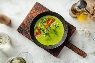 Bir kase yeşil sebze çorbası üzerine domates cipsi ve yeşillik.