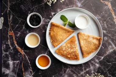 Üç üçgen krep, koyu mermer arka planda dört farklı sosla servis edilmiş.
