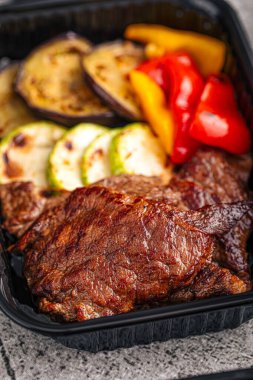 Siyah servis konteynırında sebzeli ızgara biftek.