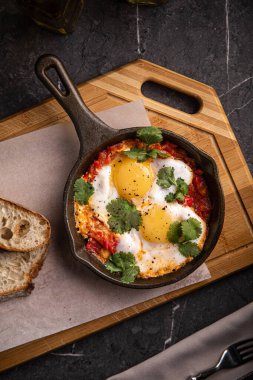 Haşlanmış yumurta ve sebzeli Shakshuka tavada ekmek ile servis edilir.