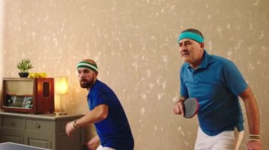 Karizmatik yaşlı adam ve arkadaşı genç adam birlikte masa tenisi oynuyorlar sağlıklı yaşam tarzının raket konseptiyle bütün topları yakalıyorlar. ARRI Alexa Mini 'de çekilen