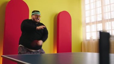 Çekici, şişman, dans eden ve hareket eden genç bir adam masa tenisi ya da masa tenisi oyununda oynamaya hazırlanıyor. En sevdiği raketini elinde tutuyor. ARRI Alexa Mini 'de çekilen