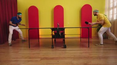 Kameranın önünde iki yakışıklı adam masa tenisi oynuyor ve yakaladıkları oyuncuya heyecanlanıyor ve topa vuruyorlar. 4k
