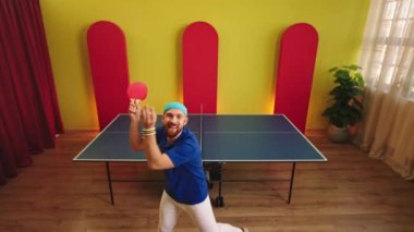 Karizmatik adam pinpon maçına başlamadan önce dans ediyor ve gülümsüyor raketi elinde tutuyor ve kameraya bakıyor..