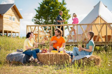 Good time for a big group of friends multiracial meeting at campsite they enjoy the time together sitting down on the haystack and make pictures for memories. Portrait