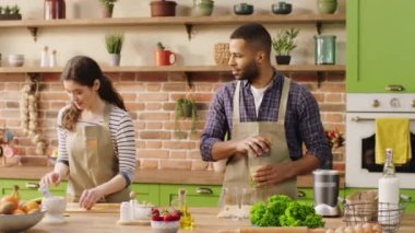 Karizmatik adam ve kız arkadaşı Avrupalı mutfaktaki adaya bakıyorlar birlikte sağlıklı bir kahvaltı hazırlıyorlar miksere taze meyve ekliyorlar ve sağlıklı bir meyve suyu karıştırıyorlar. 4k