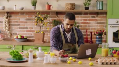 Mutfak adasında bilgisayarını ve kredi kartını kullanarak internetten ödeme yapan yakışıklı bir adam..