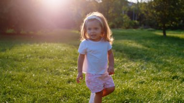 Parkın ortasında çimlerin üzerinde koşan sevimli küçük kız doğadan mutlu ve heyecanlı..