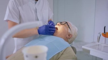 Yaşlı bir hastanın diş hekiminde çek randevusu var. Diş hekimi, diş aletlerini kullanarak diş doktorunu muayene ediyor. Dosyalamayla ilgili sorunları kontrol ediyor..