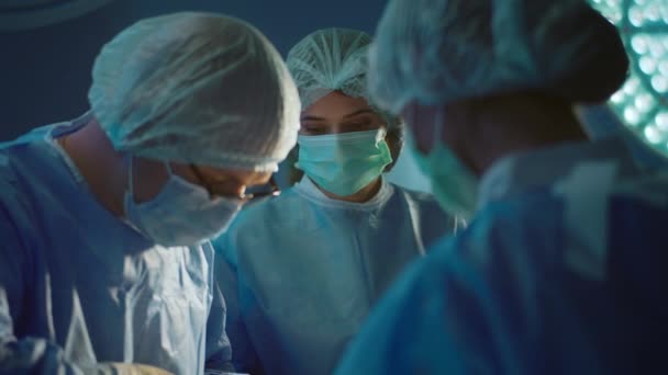 完全な外科医の制服を着た男性医師が激しい手術をしています彼の両側に2人のアシスタントが彼を助けています — ストック動画
