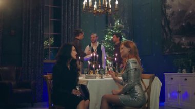 Noel yemeği kameranın önünde güzel ve harika görünümlü kadınlar arka plandaki yemek masasında otururken tartışıyor erkekler Noel ağacının yanında tartışıyorlar. 4k