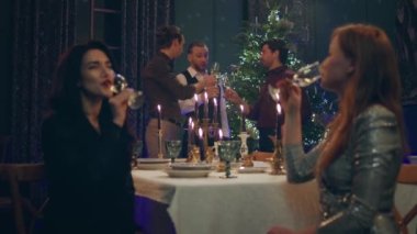 Noel ya da yeni yıl atmosferi yemek masasında iki çekici bayan oturmuş şampanya içerken erkekler Noel ağacının yanında tartışırlar..