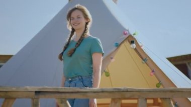 Çadırdan çıkıp kamp alanında yürüyen kırsal görünüşlü bir bayan sabah büyük bir gülümsemeyle doğada bu yerde aşık olduğunu hissediyor. 4k