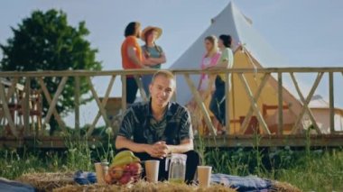 Kameraya poz veren yakışıklı bir adam yaz günü kamptaki samanlıkta otururken tatlı tatlı gülümsüyor. 4k