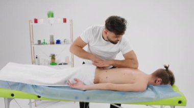 Geniş masaj odasındaki adamın rahat bir sırt masajı var profesyonel terapist yoğun bir masaj yapıyor. 4k