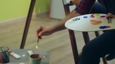 A painter handsome man is painting very carefully something beautiful on a big canvas in his art room.