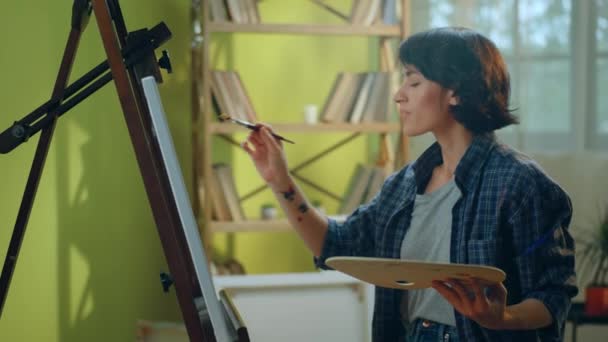 一个美丽的女人 她是一个画家 手上沾满了颜料 当她坐在凳子上的时候 正在她面前的一张大帆布上画什么东西 — 图库视频影像
