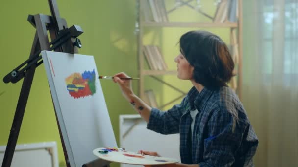 美しい画家の女性は 彼女のすでに素晴らしい芸術作品に小さな詳細を追加し それが彼女のアートスタジオのアパートにいる間 それがさらに良く見えるようにするためにそれに取り組んでいます Arri Alexaで撮影 — ストック動画