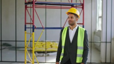 In the luminous industrial building charismatic man architect walking to the camera then posing smiling large and crossing hands he wearing protective equipment. 4k